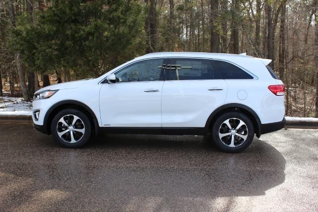 a white car parked in a parking lot next to some trees and snow covered ground