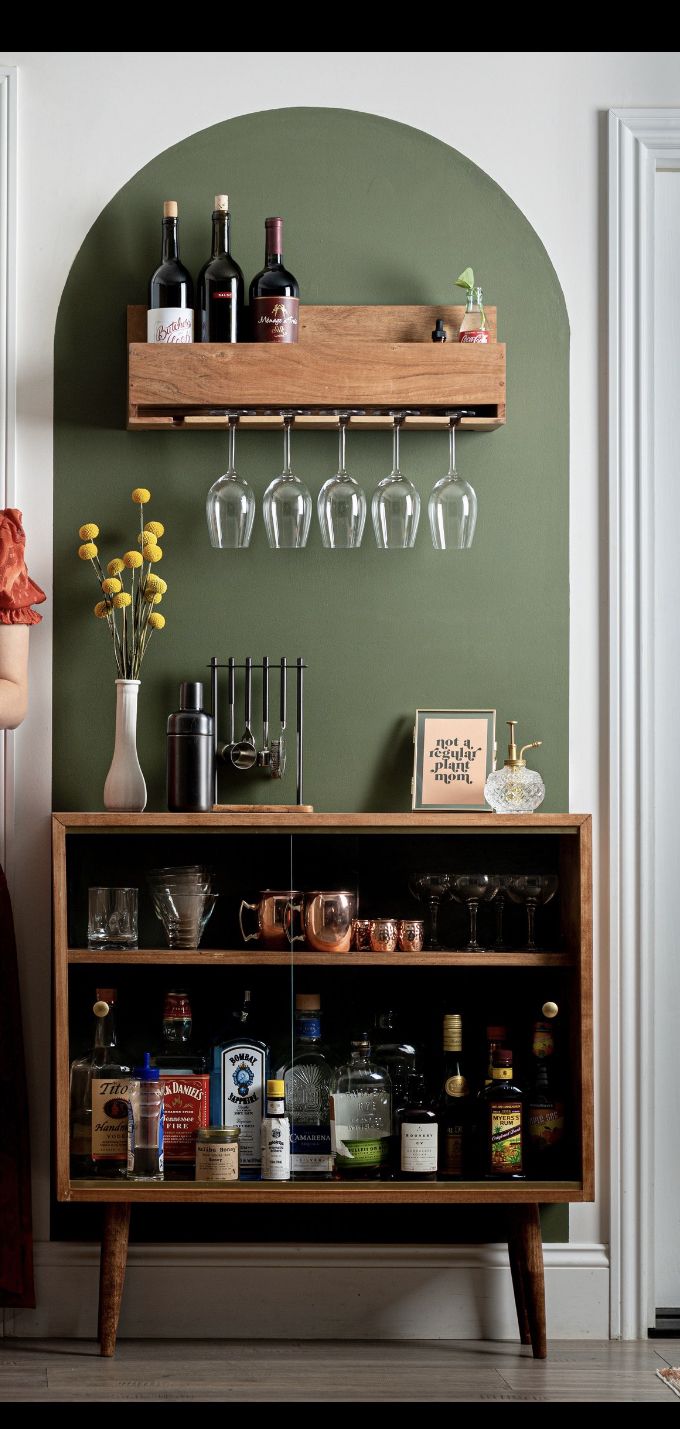 a bar with wine glasses and liquor bottles on the top shelf, next to a vase filled with flowers