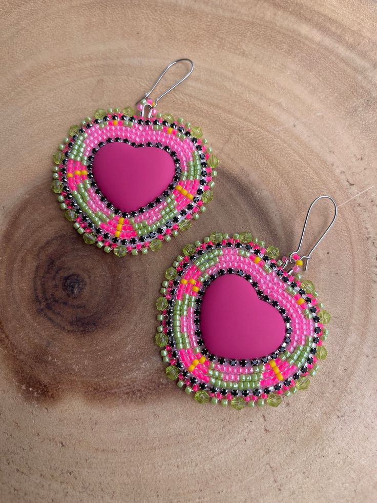 pair of pink and green beaded earrings with heart shaped design on wooden background, closeup