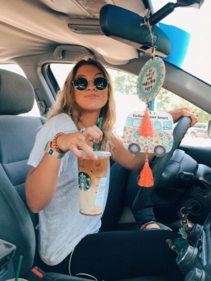 a woman sitting in the driver's seat of a car holding up a drink