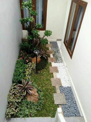 a narrow garden area with plants and rocks in the grass next to an open door