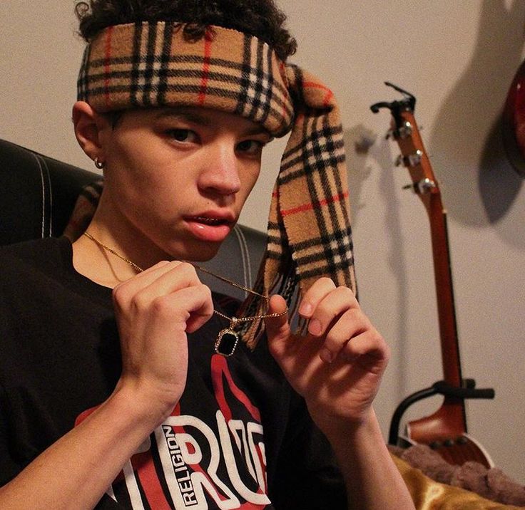 a young man wearing a plaid bandana and looking at the camera while holding his tie up to his head