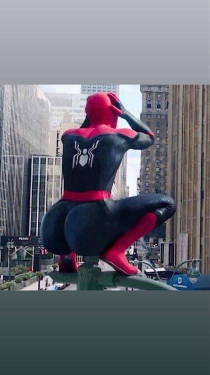 a spider man statue sitting on top of a pole in the middle of a city