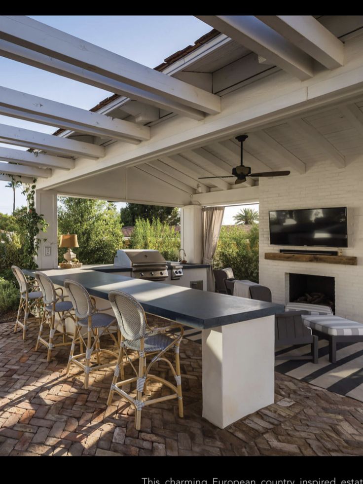 an outdoor kitchen and dining area with brick pavers flooring, white painted walls and ceiling fans