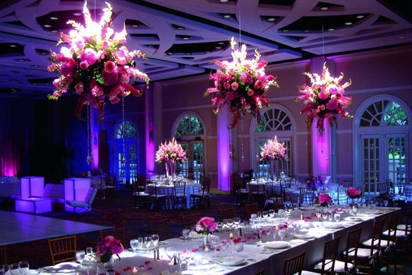 the tables are set with white linens and pink flowers in vases hanging from the ceiling