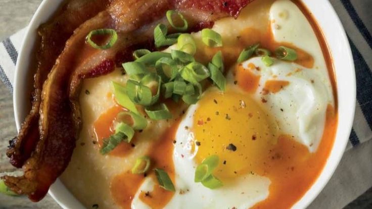 a white bowl filled with eggs, bacon and gravy on top of a table