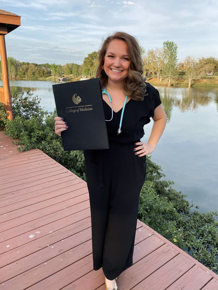 a woman standing on a dock holding up a passport and smiling at the camera with her hands in her pockets