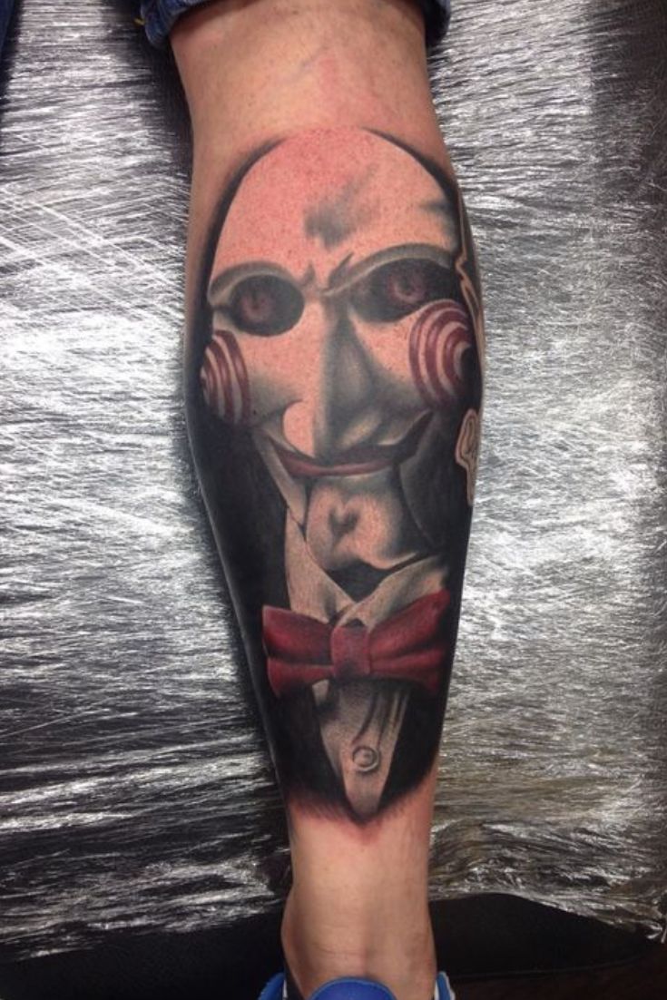 a man's leg with a mask and bow tie tattoo on the calf area