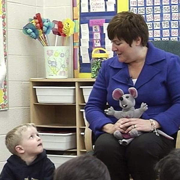 a woman sitting in front of a group of children with stuffed animals on her lap