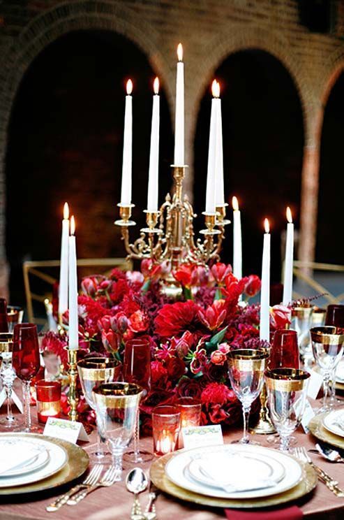 the table is set with red flowers and white plates, silverware, and candles