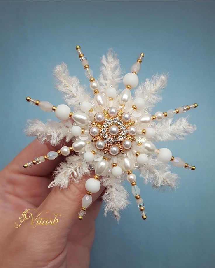 a hand holding a snowflake with pearls and beads