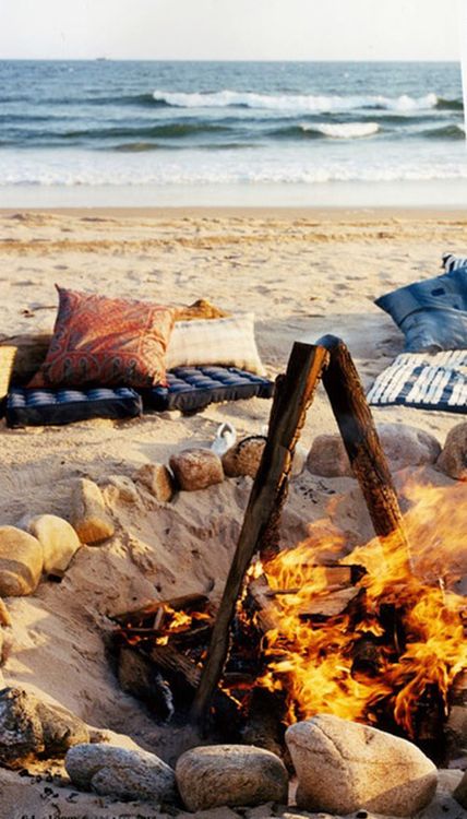 a campfire on the beach with pillows and blankets