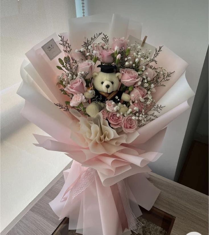 a teddy bear is sitting on top of some pink flowers and greenery in a bouquet