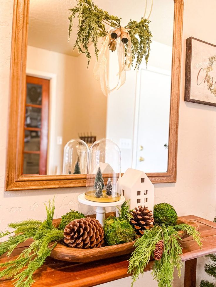 pine cones and greenery sit on top of a wooden table in front of a mirror