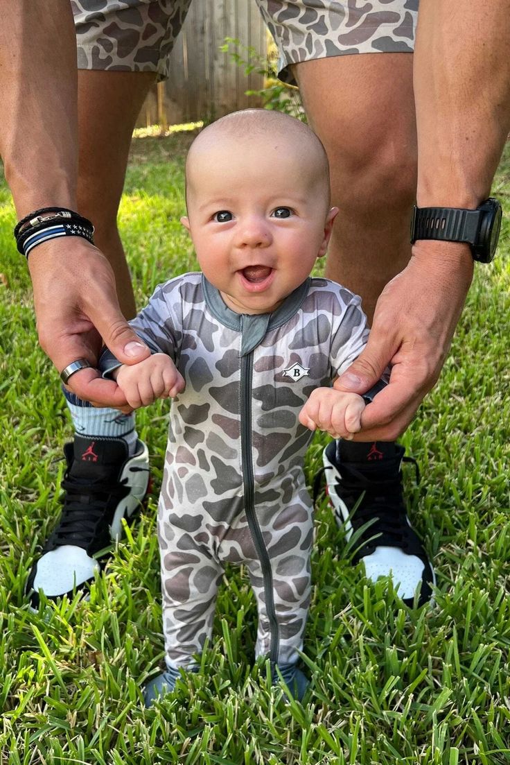 a man holding the hands of a baby in front of him on some green grass