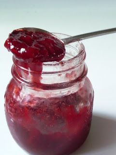 a jar filled with raspberry jam sitting on top of a white table next to a spoon