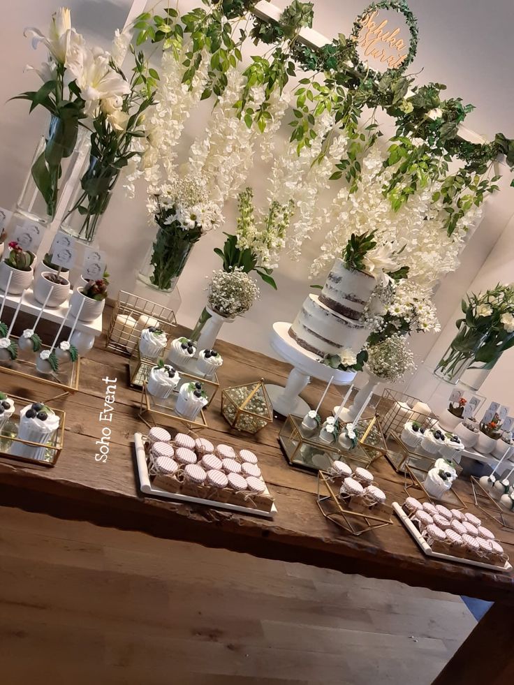 a table topped with cakes and cupcakes next to tall vases filled with flowers