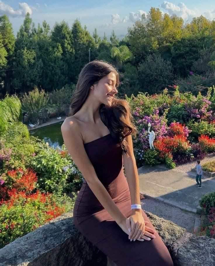 a woman sitting on top of a stone wall next to colorful flowers and greenery