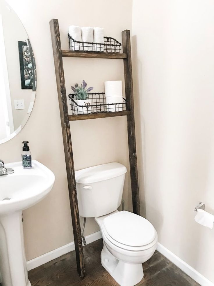 a white toilet sitting next to a bathroom sink under a wooden shelf filled with items