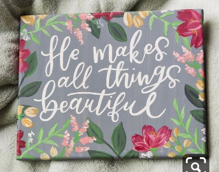 a painted sign that says he makes all things beautiful on grey background with pink and yellow flowers