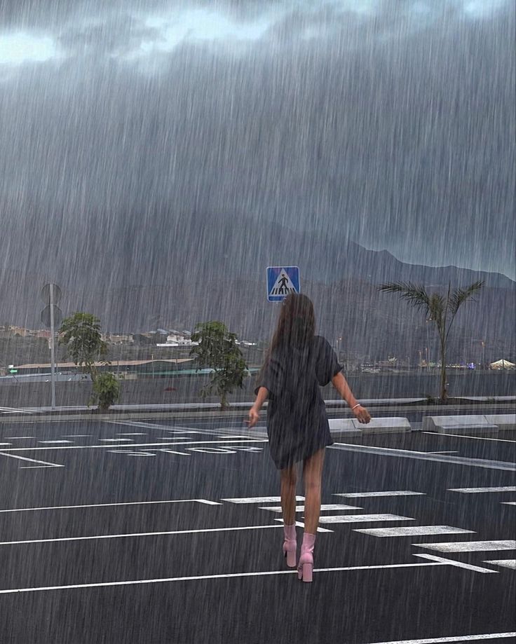 a woman walking across a parking lot in the rain