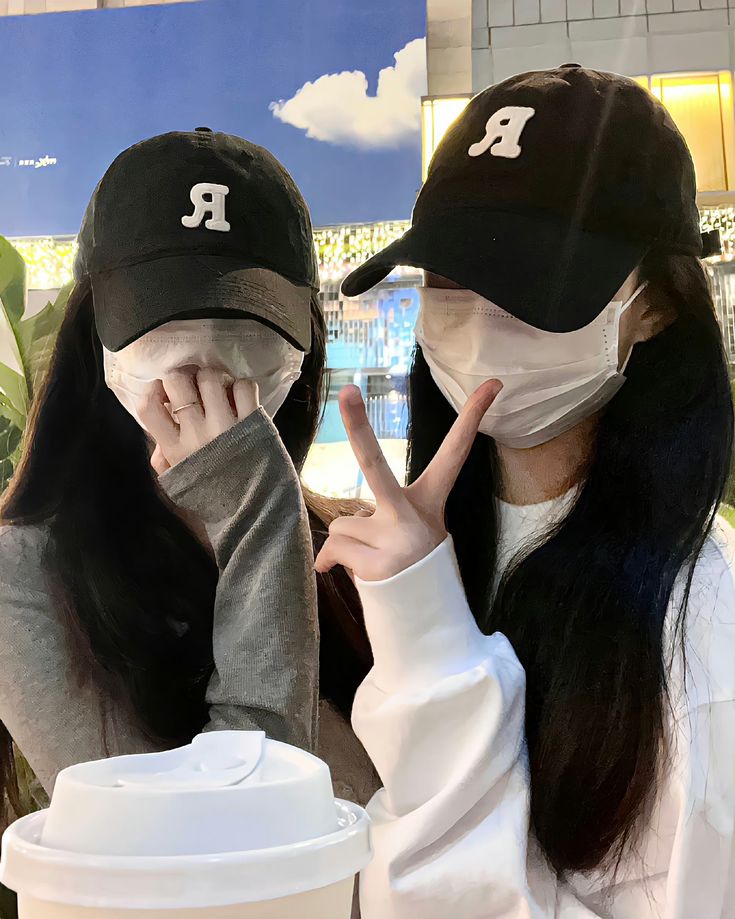 two women wearing face masks and holding up peace signs in front of a coffee cup