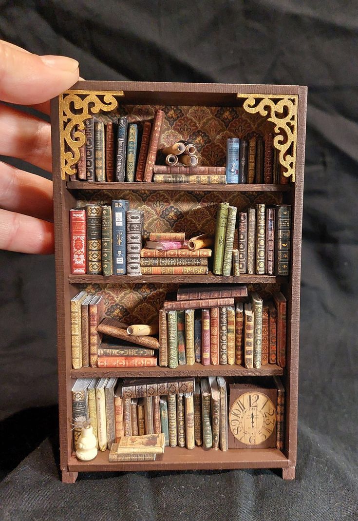 there is a miniature book shelf with many books on it and a clock in the middle