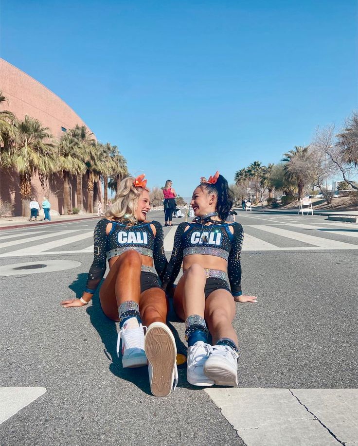 two cheerleaders sitting on the ground with their legs crossed