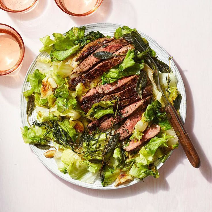 a white plate topped with meat and lettuce next to two glasses of wine