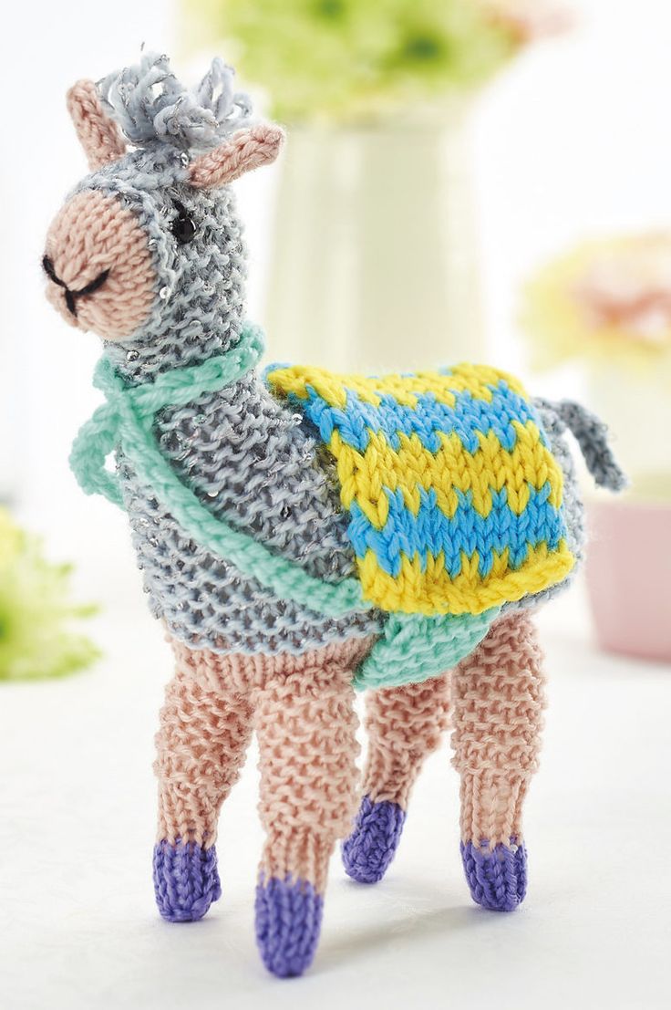 a crocheted llama with a sweater on it's back standing in front of a vase