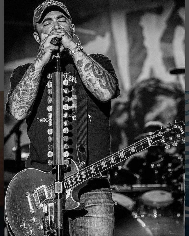 a black and white photo of a man with tattoos on his arm holding a guitar