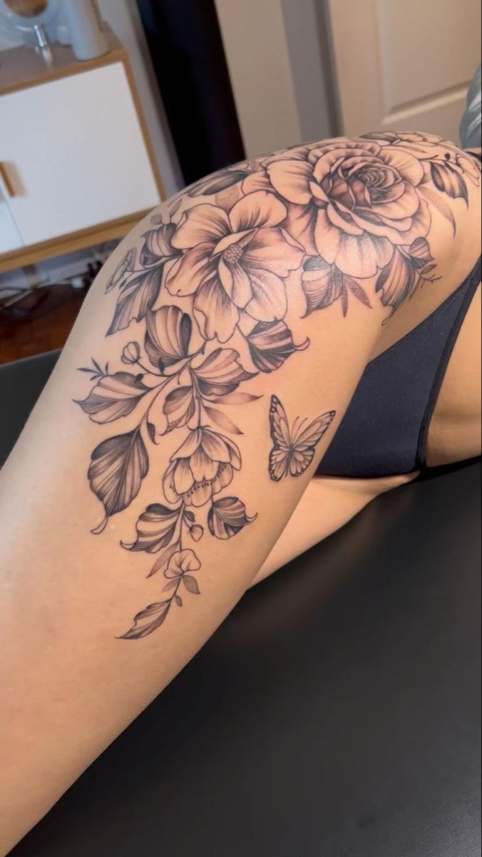 a woman laying on top of a black table next to a flower and butterfly tattoo