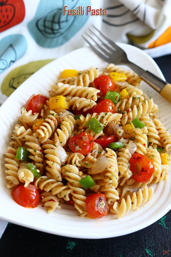 a white plate topped with pasta and veggies next to a knife and fork