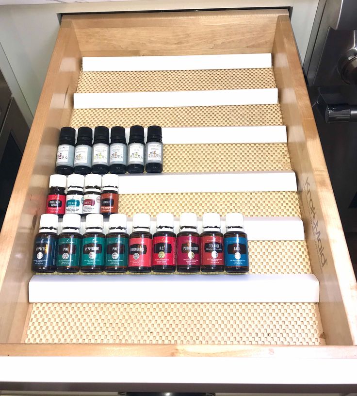 bottles of essential oils are lined up in a drawer on the counter top, with one shelf full of them