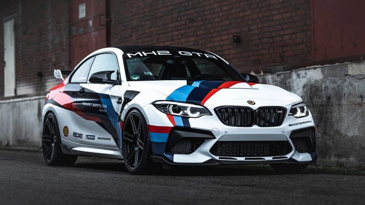 a white car with colorful stripes parked on the street next to a brick wall in front of a building