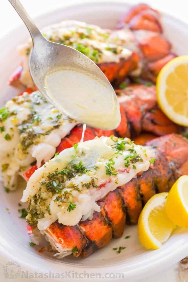 lobster with lemon wedges and parsley sauce on a white plate, ready to be eaten