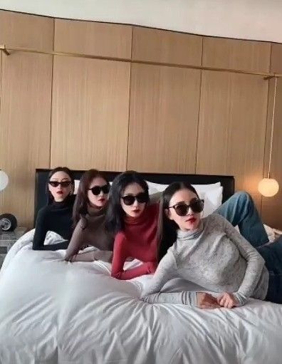 four people sitting on a bed with sunglasses on their heads and one person laying down