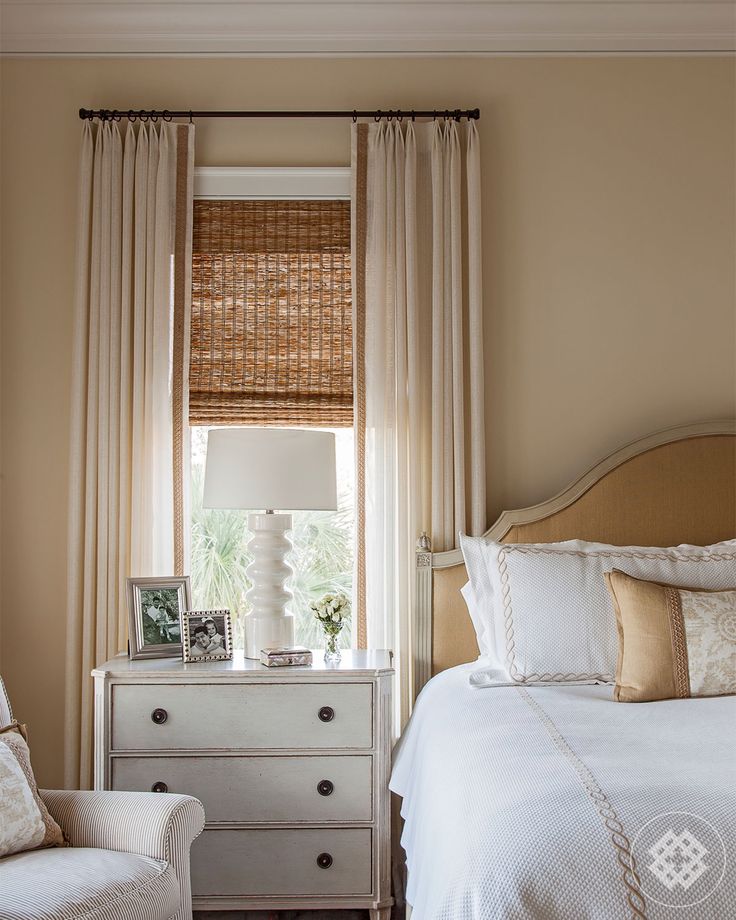 a white bed sitting next to a window in a room with beige walls and curtains