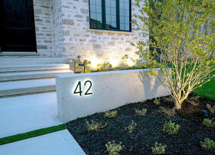 a house number sign is lit up in front of a small tree and landscaping area