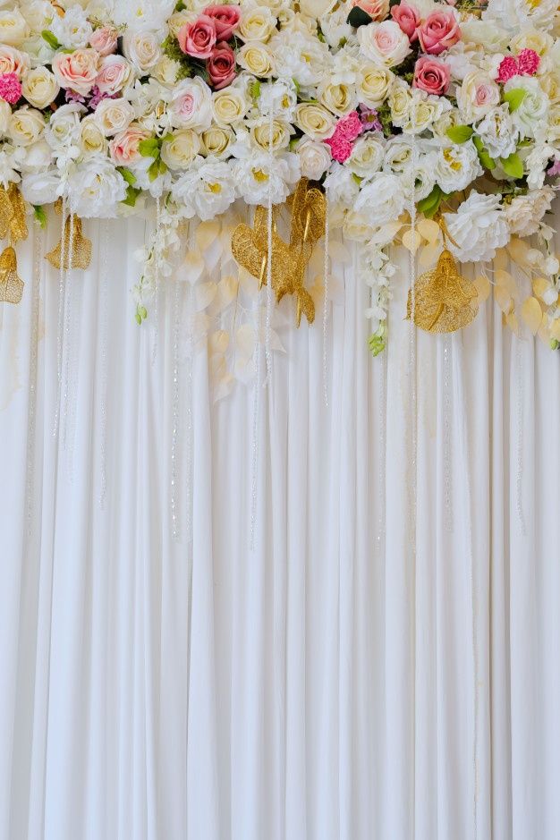 an arrangement of flowers on the back of a white drape with gold bow ties