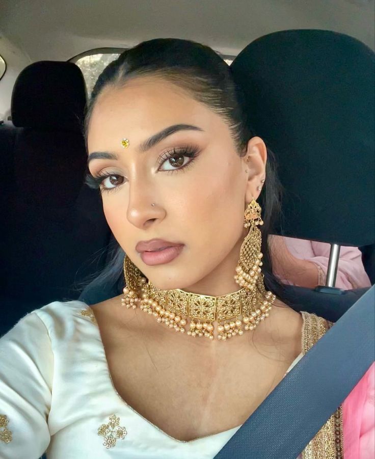 a woman in a car wearing a gold choker and matching necklace with large earrings