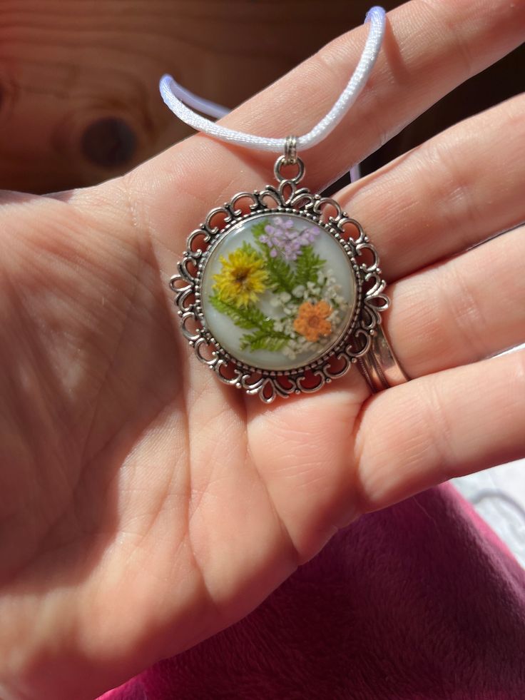 a woman's hand is holding a necklace with an image of flowers on it