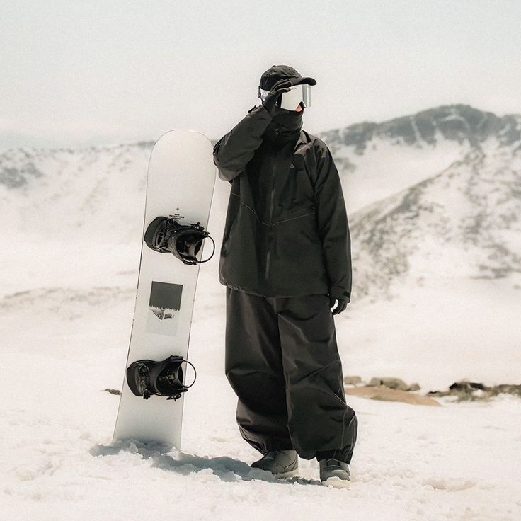 a man standing in the snow holding a snowboard on his head and covering his eyes