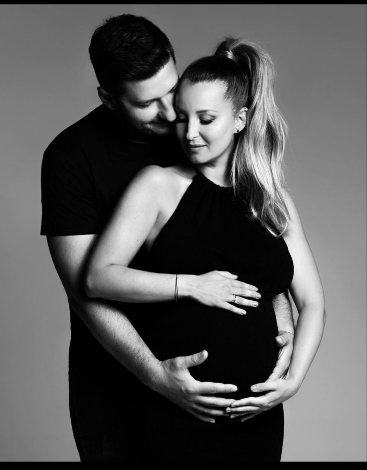 a man and woman embracing each other in black and white, with their arms around the pregnant belly