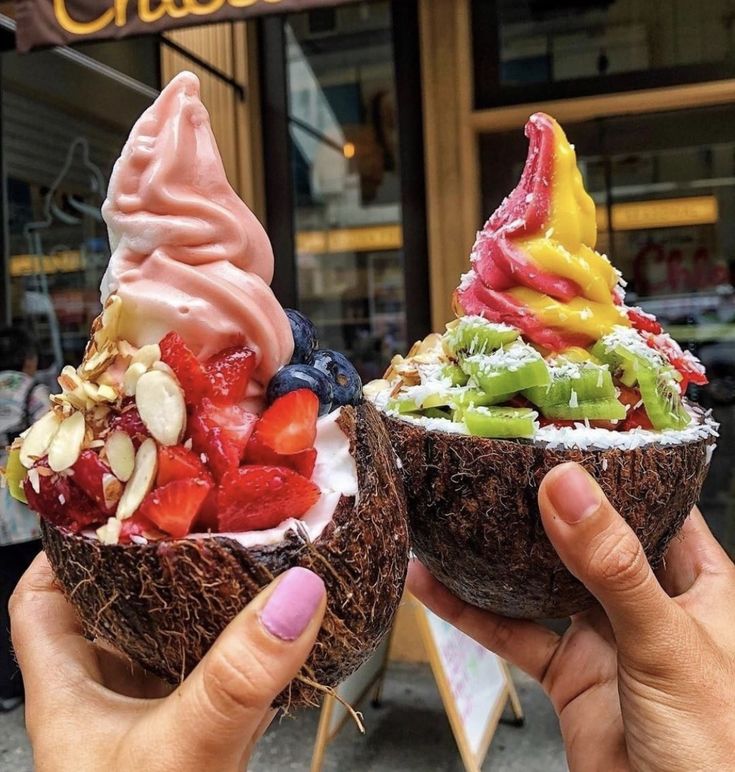 two people holding up coconut bowls filled with ice cream and fruit