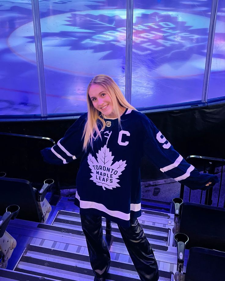 a woman standing in front of an ice rink wearing a hockey jersey and black leather pants