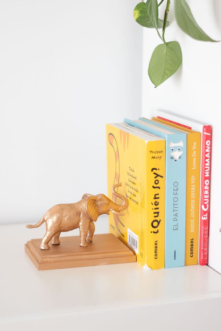 a small elephant figurine sitting on top of a book shelf next to two books