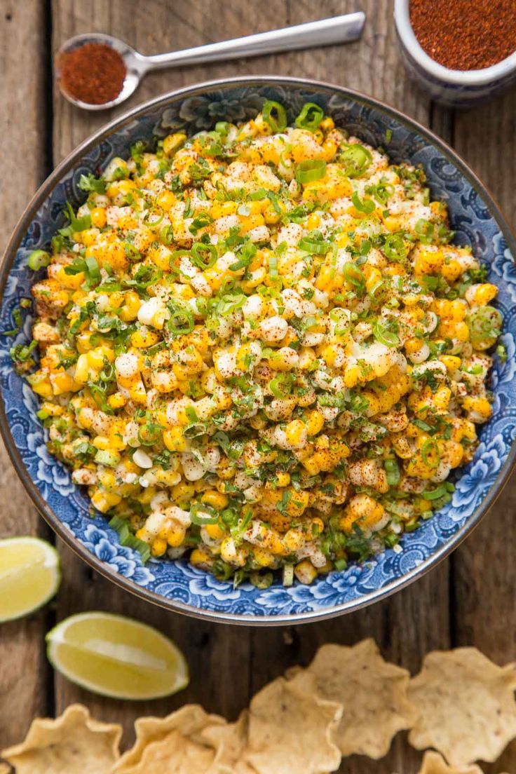 a bowl filled with corn and green onions next to some tortilla chips on a wooden table