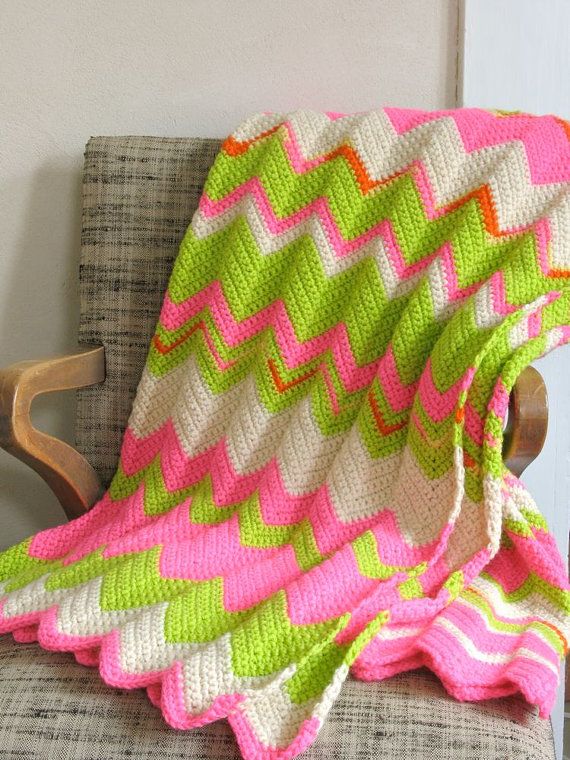 a pink and green blanket sitting on top of a chair next to a wooden rocking chair