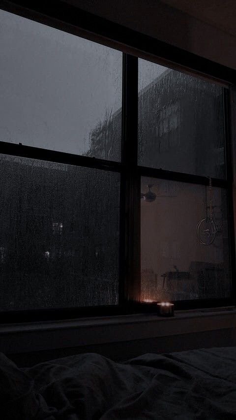 a dark room with a window that has rain falling on the windows and lights shining in it